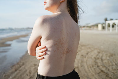 Midsection of shirtless woman standing at beach