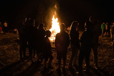 People standing by bonfire at night