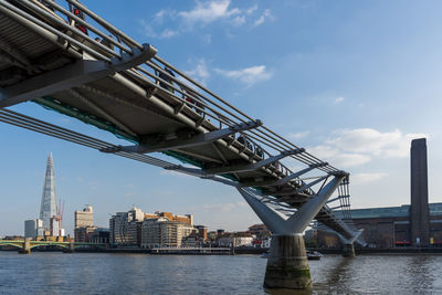 Low angle view of millennium bridge over river by buildings against sky.  view to tate modern. 