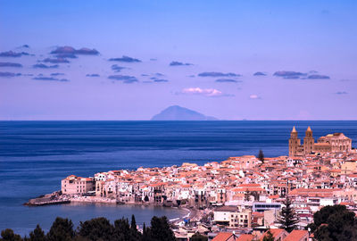 Buildings by sea against blue sky