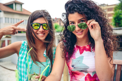 Portrait of happy friends wearing sunglasses while sitting at sidewalk cafe