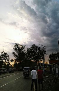 Rear view of people walking on road against cloudy sky