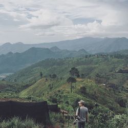 Rear view of man with camera looking at mountains against sky