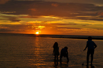 Silhouette people on beach against sky during sunset