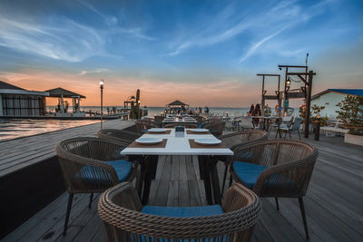 Empty chairs and tables at restaurant against sky during sunset