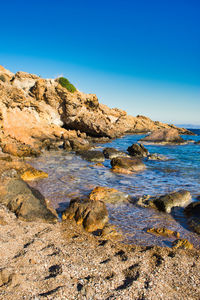 Rocks in sea against clear blue sky