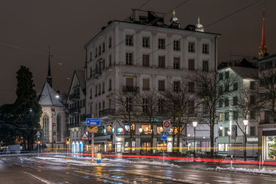 Light trails on road against buildings at night