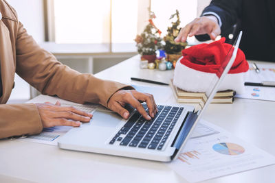 Midsection of businessman using calculator while colleague writing on graph with christmas decorations on table