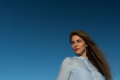 Low angle view of beautiful woman against clear blue sky