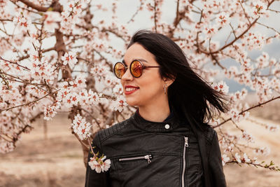 Beautiful young woman standing by cherry blossom tree