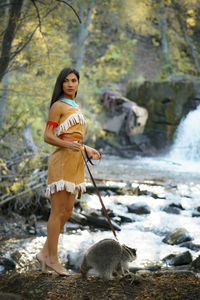 Young woman in traditional clothing looking away while standing by raccoon in forest