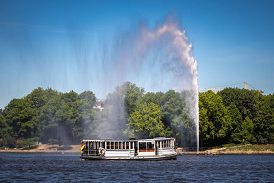 Boat in lake alster with fontäne against sky