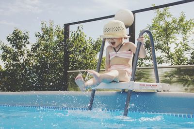 Full length of woman jumping in swimming pool against sky