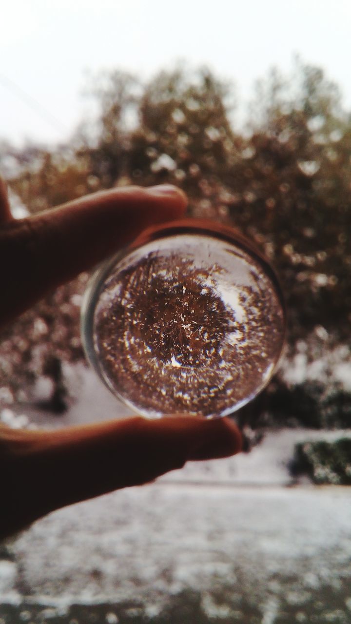 CLOSE-UP OF HAND HOLDING CRYSTAL BALL AGAINST SKY