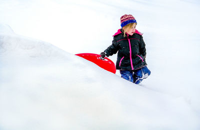 Adorable little girl walks through the snow with her red sled