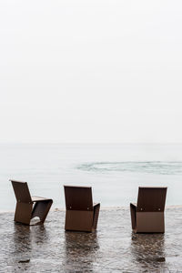 Empty chairs on promenade by sea against clear sky