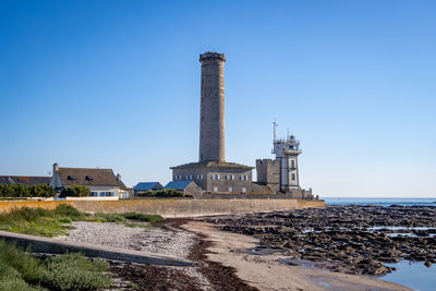 Lighthouse by sea against clear blue sky