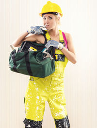 Portrait of female worker in coverall holding tool bag while standing against wall