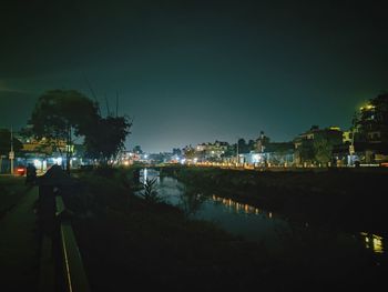 Illuminated buildings by lake against sky in city at night