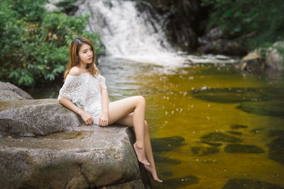 Young woman looking away while sitting on rock