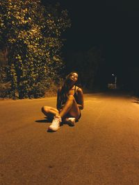 Full length of young woman sitting on road at night