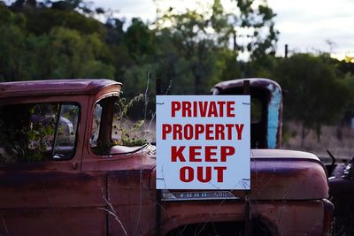 Warning sign at an ild scrapyard with cars of the fifties. private property keep out.