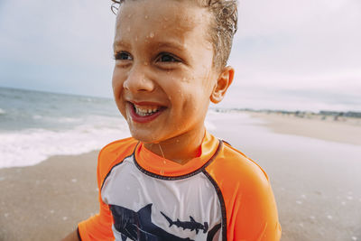 Cheerful wet boy looking away at beach against sky