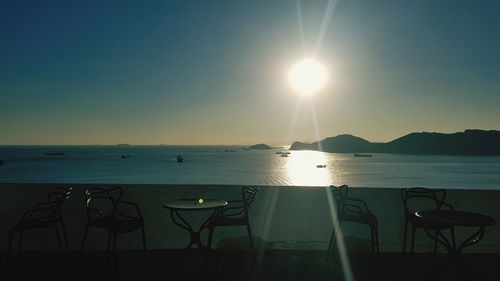 Chairs and table by sea against sky during sunset