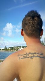 Side view of man relaxing at sea shore against sky