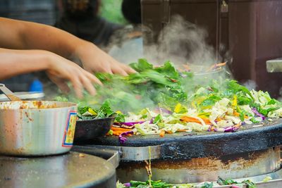 Cropped image of vendor hand cooking vegetables in market