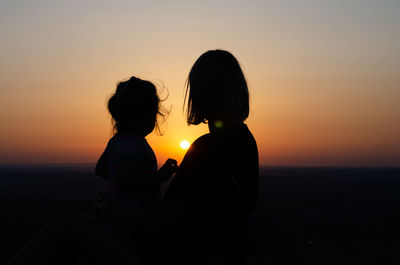 Silhouette woman with arms raised against sky during sunset