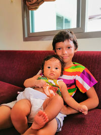 Portrait of a smiling boy with little baby sitting at home