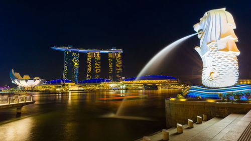 Illuminated fountain in city against sky at night