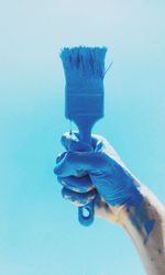 Close-up of hand holding paintbrush against blue background