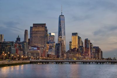 One world trade center by hudson river against sky in city at dusk