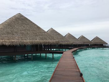 Thatched roof huts on pier against cloudy sky