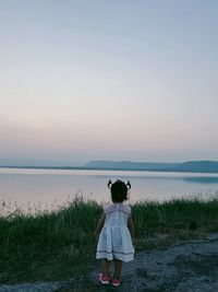 Rear view of woman standing on shore against sky