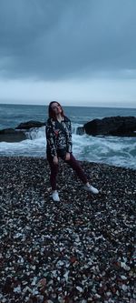 Full length of boy on pebbles at beach against sky