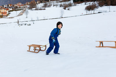 Smiling girl with short dark hair pulling up the wooden sled in snowy mountain