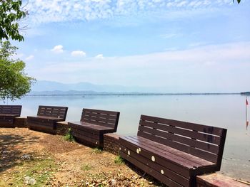 Empty bench by sea against sky