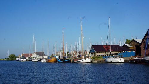 Sailboats moored at harbor against clear blue sky