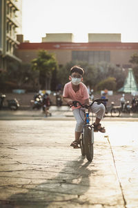 Rear view of kid riding bicycle on street, against the sunlight