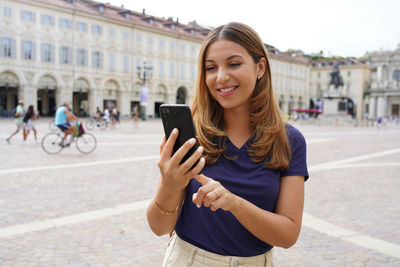 Portrait of a beautiful smiling modern girl using a mobile phone on old town square