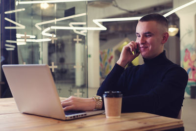 Young man using mobile phone while sitting on table