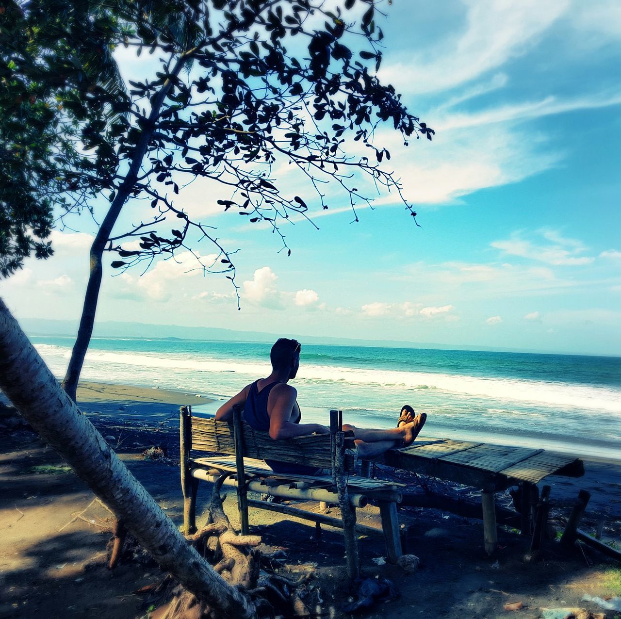 WOMAN SITTING ON SEAT BY SEA AGAINST SKY