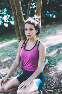 Portrait of teenage girl sitting by tree trunk