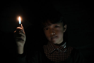 Portrait of girl holding illuminated cigarette lighter in darkroom