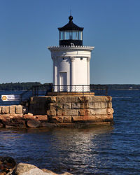 Lighthouse by sea against clear sky