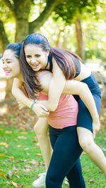 Happy young woman giving piggyback to friend at park
