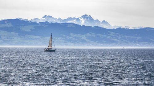 Sailboat sailing on sea by mountain against sky